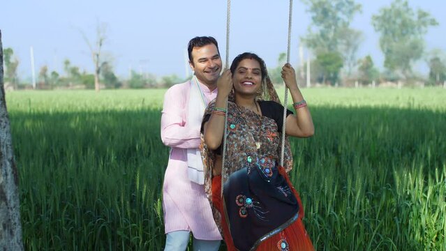 Indian village couple happily enjoying their leisure time on a swing - family time  quality time  husband-wife love  village lifestyle. Indian farmer spending quality time with his wife in village ...
