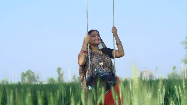 Young village woman enjoying her leisure time on a swing - happy woman  mother  daughter in law  bahu  saree  traditonal wear. Indian woman in traditional wear swinging - village  relaxing  rural l...