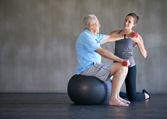 Physiotherapist, dumbbells and smile of senior man on ball for fitness or rehabilitation at gym on...