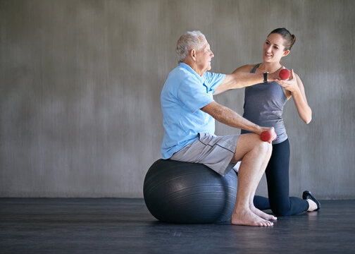 Physiotherapist, dumbbells and smile of senior man on ball for fitness or rehabilitation at gym on mockup. Elderly person, weightlifting and personal trainer help for body health or physical therapy