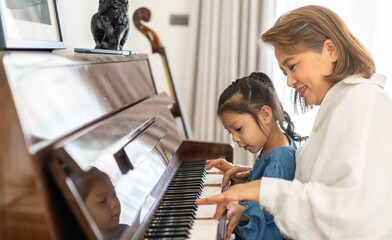 Portrait of happy love asian grandmother and asian cute girl play and enjoy relax teaching and play piano music lesson at home.senior, insurance, care.girl with their laughing grandparents.Family
