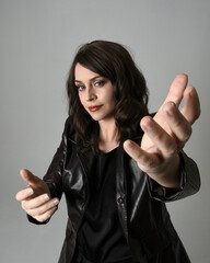 close up portrait of beautiful brunette woman wearing long black leather trench coat. Gestural hand poses, arms reaching towards camera, with wide angel perspective, Isolated on studio background