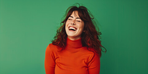 Obraz premium A cheerful young woman with a nose ring, wearing an orange sweater, laughing against a green background, exuding happiness and positive vibes.