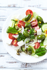 Healthy Salad with Feta Cheese, Green Olives, Baby Spinach, Cucumber, Cherry Tomatoes and Capers. Bright background. Top view. Close up.	