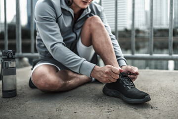 A man tying shoelaces on sport shoes in the city center park before cardio workout, running.  Health and Lifestyle in big city life concept. - obrazy, fototapety, plakaty
