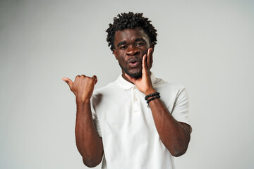 Young African Man Pointing at Something Against Gray Background