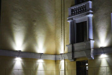 lamps illuminating of the wall of the house with decorative columns and a balcony at night