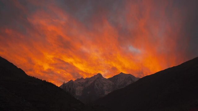Fiery red sunset sky over snow capped Himalaya mountains at Keylong, Lahaul, India. Orange color clouds in sky. Scene of Colorful romantic red sky sunset over mountains.