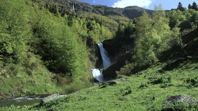 Lateral camera translation movement. General view of the double waterfall and the green environment and mountains. 'Saut deth Pish' in the Aran Valley (Catalan Pyrenees)