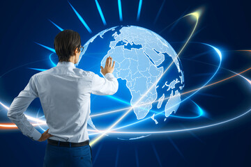 Back view of young man using glowing futuristic blue globe hologram on blurry background. Digital...