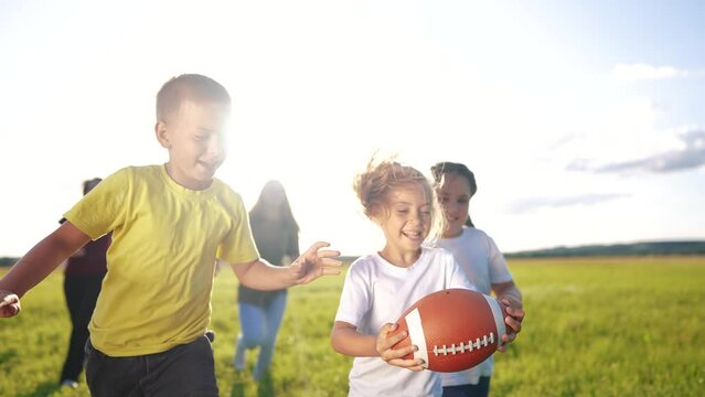children playing rugby in the park. a group of children play american football run outdoors in the park in summer. happy family kid dream concept. family lifestyle children play american football run