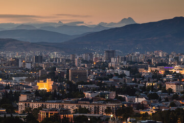 View of Tbilisi from the surrounding hills. In the background you can see the Caucasus Mountains. A warm autumn day in the capital of Georgia. - obrazy, fototapety, plakaty