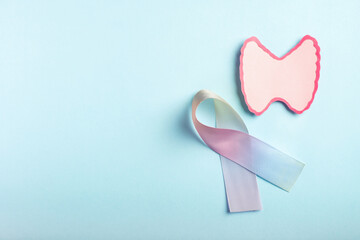 Thyroid gland cancer awareness concept. Thyroid decorative model and colorful ribbon on pastel blue background. Top view, copy space