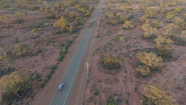 Drone clipe showing road train and vehicles driving along straight road through desert landscape