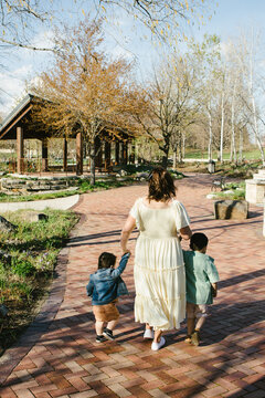 Mother walks through garden park holding sons hands