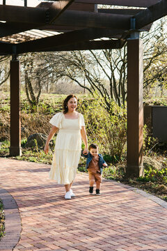 Mom walks down brick path holding toddler son hand in garden