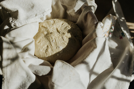 Bread proofs in bowl with tea towel on kitchen counter in sunshine