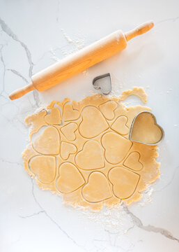 Top view of cookie dough cut into heart shapes on marble counter.