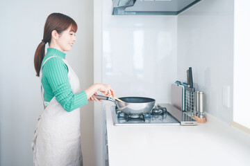 キッチンでフライパンを使って料理する女性