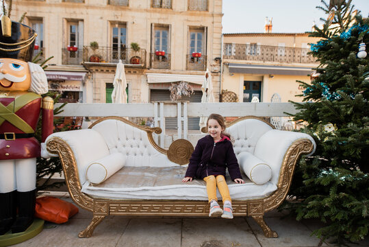 Little girl sits on decorated Christmas couch at December market