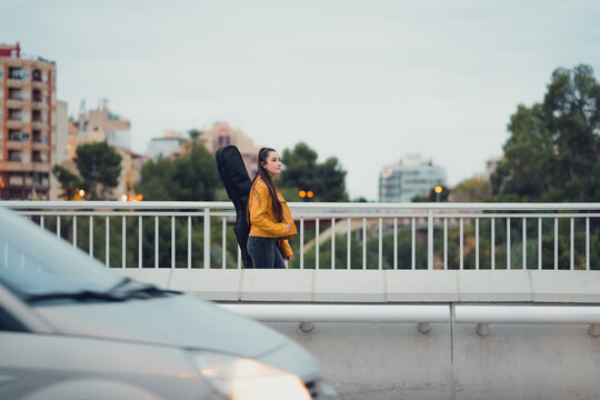 Young woman carrying guitar on her back walking across urban bridge