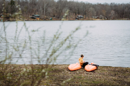 Boy sitting on kayak on lake shore fishing