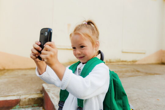 A little girl with a backpack takes a photo on her smartphone