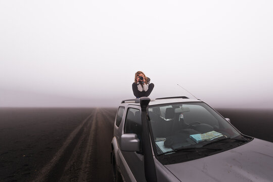 Woman standing on roof of car while taking pictures highlands iceland