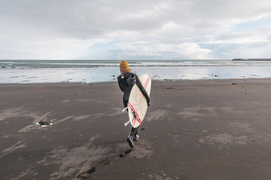 Woman walking on beach with surf board winter iceland