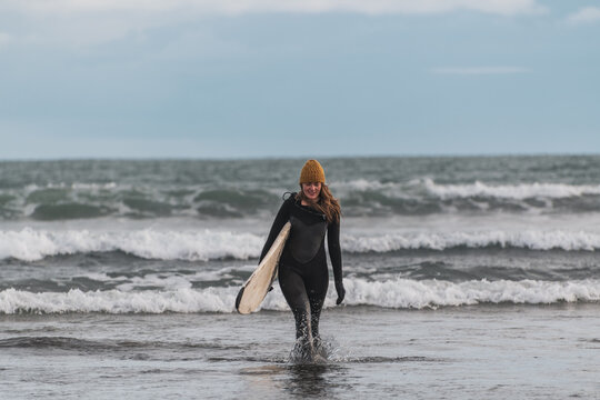 Woman walking on beach with surf board winter iceland