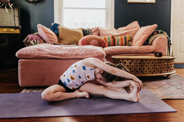 Wide shot of young girl stretching on purple yoga mat in living room