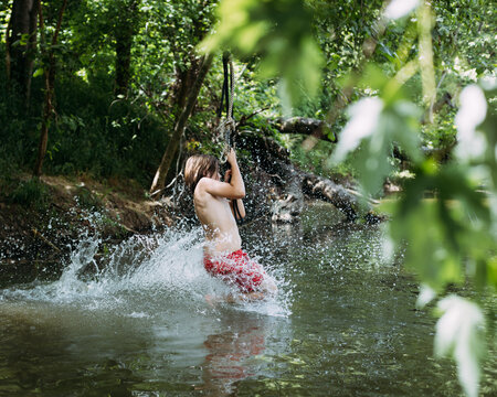 Child splashing into water from rope swing during summer