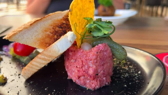 Delicious beef steak tartare with toast bread and a pickle on a plate, raw meat dish, 4K shot