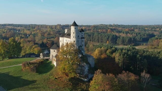 The grand silhouette of a medieval fortress towers over a forest ablaze with autumn's vibrant colors. Bobolice, Polish Jura, Polish Jurrasic Haighland, Poland