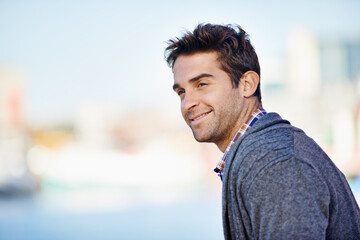 Fototapeta premium Man, smile and mockup for outdoor and trip for travel or walk in urban or city with joy. Young person with joy and jacket and looking for view, comfort and relax for break and isolated aesthetic