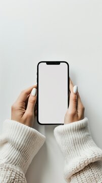 A woman is holding a phone with a white background. The phone is black and has no screen. The woman's hands are wrapped around the phone, and she is looking at it