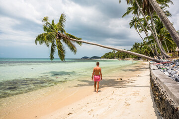 Mężczyzna w kąpielówkach na rajskiej plaży pod palmą