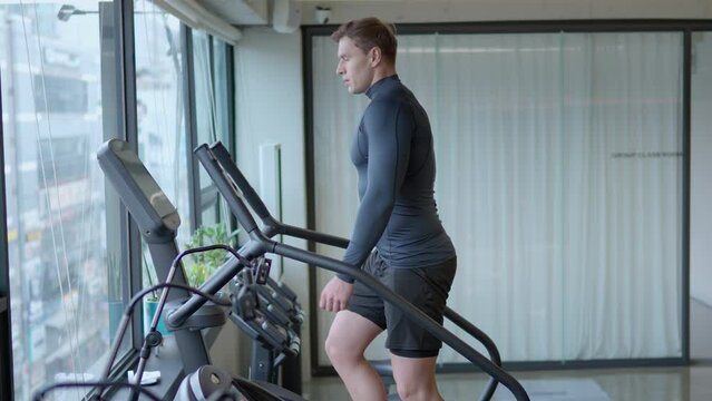 Athletic Man Exercises on Stepmill Stair Climber Machine in Modern Gym Looking Though Window On City Street in slow motion