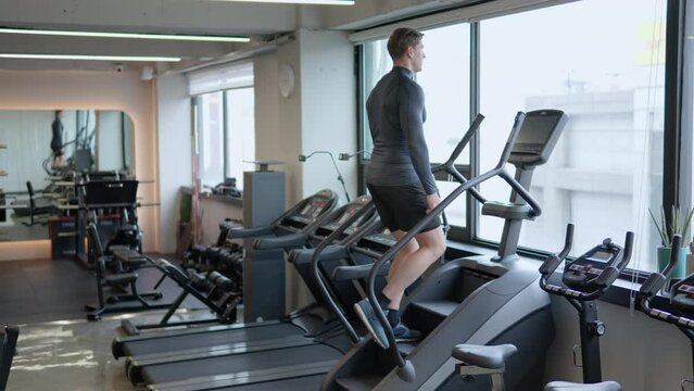 Man athlete in 30s using stair climbing machine to burn calories in empty gym