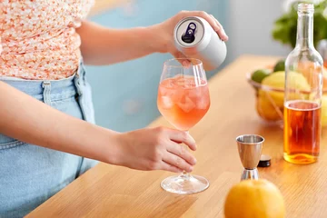 Foto op Canvas drinks and people concept - close up of woman pouring soda from tin can to wine glass and making orange cocktail at home kitchen © Syda Productions