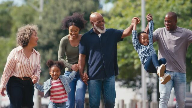 Three generation family walking outdoors laughing and playing with grandchildren together - shot in slow motion