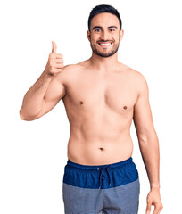 Fototapeta premium Young handsome man wearing swimwear smiling happy and positive, thumb up doing excellent and approval sign