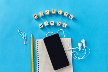 digital detox and technology concept - smartphone, earphones and wooden toy block or stamps on blue background - 767716731
