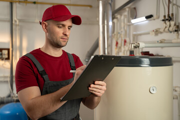A focused technician wearing a red cap and overalls is carefully inspecting an industrial boiler....