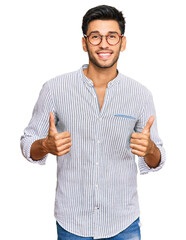 Young handsome man wearing casual clothes and glasses success sign doing positive gesture with hand, thumbs up smiling and happy. cheerful expression and winner gesture.