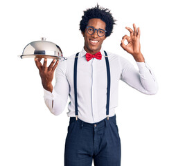 Handsome african american man with afro hair wearing waiter uniform holding silver tray doing ok...