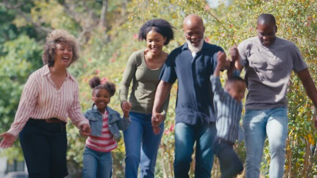Three generation family walking outdoors laughing and playing with grandchildren together - shot in real time