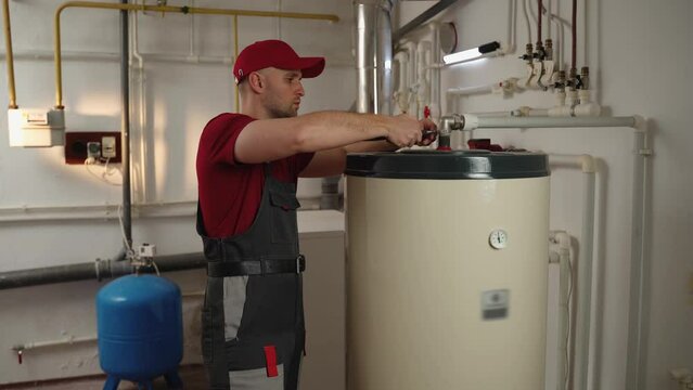 A professional technician wearing a red uniform is diligently working on maintaining a boiler in a residential utility room, ensuring the system operates efficiently and safely for the home.