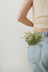 Young pretty woman with chamomile flowers bouquet in jeans pocket