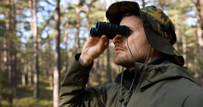 man in camouflage clothing looking through binoculars in forest